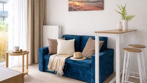 A blue sofa with a white radiator, a small table with a cup, a hat, and a plant on a white stand. - HoliApart Trimare Billard &Seasonal Pool (Sztutowo)