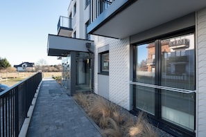 A modern building with a glass entrance, a metal railing, and a pathway with dry grass. - HoliApart Trimare Billard &Seasonal Pool (Sztutowo)