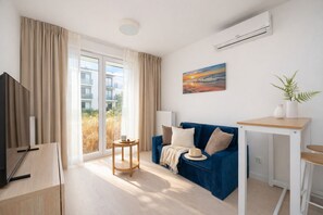 A modern hotel room with a blue sofa, a small table, a TV, and a large window with curtains. - HoliApart Trimare Billard &Seasonal Pool (Sztutowo)