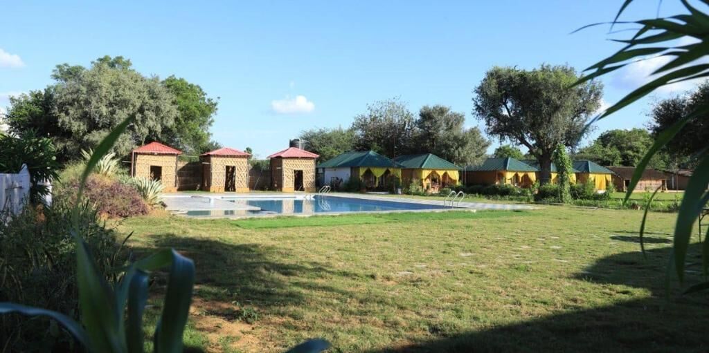 A pool area with a clear sky, surrounded by small buildings with red roofs, likely part of a resort or hotel.
