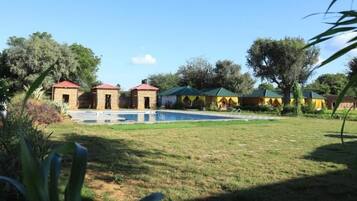 A pool area with a clear sky, surrounded by small buildings with red roofs, likely part of a resort or hotel.