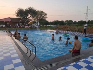 A swimming pool with people enjoying the water, a checkered floor, and a water fountain.