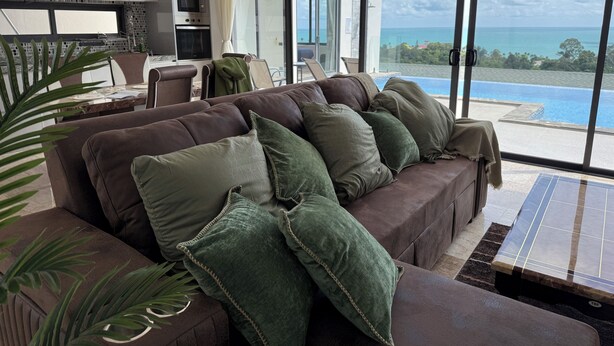 A modern living room with a brown leather sofa, green cushions, and a large window overlooking a pool and ocean. - Top Sea view villa Josephine. Close to Chaweng beach (Koh Samui)