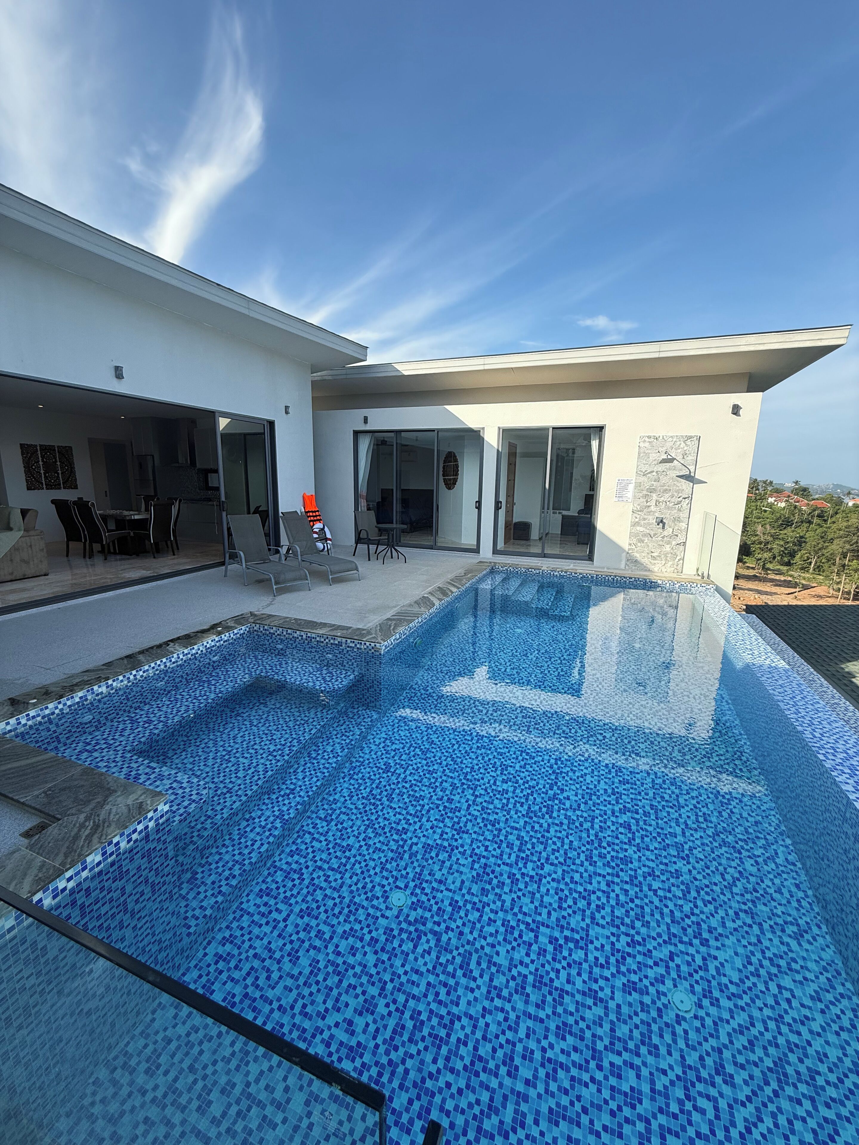 A modern house with a swimming pool, outdoor seating, and a view of the landscape.
