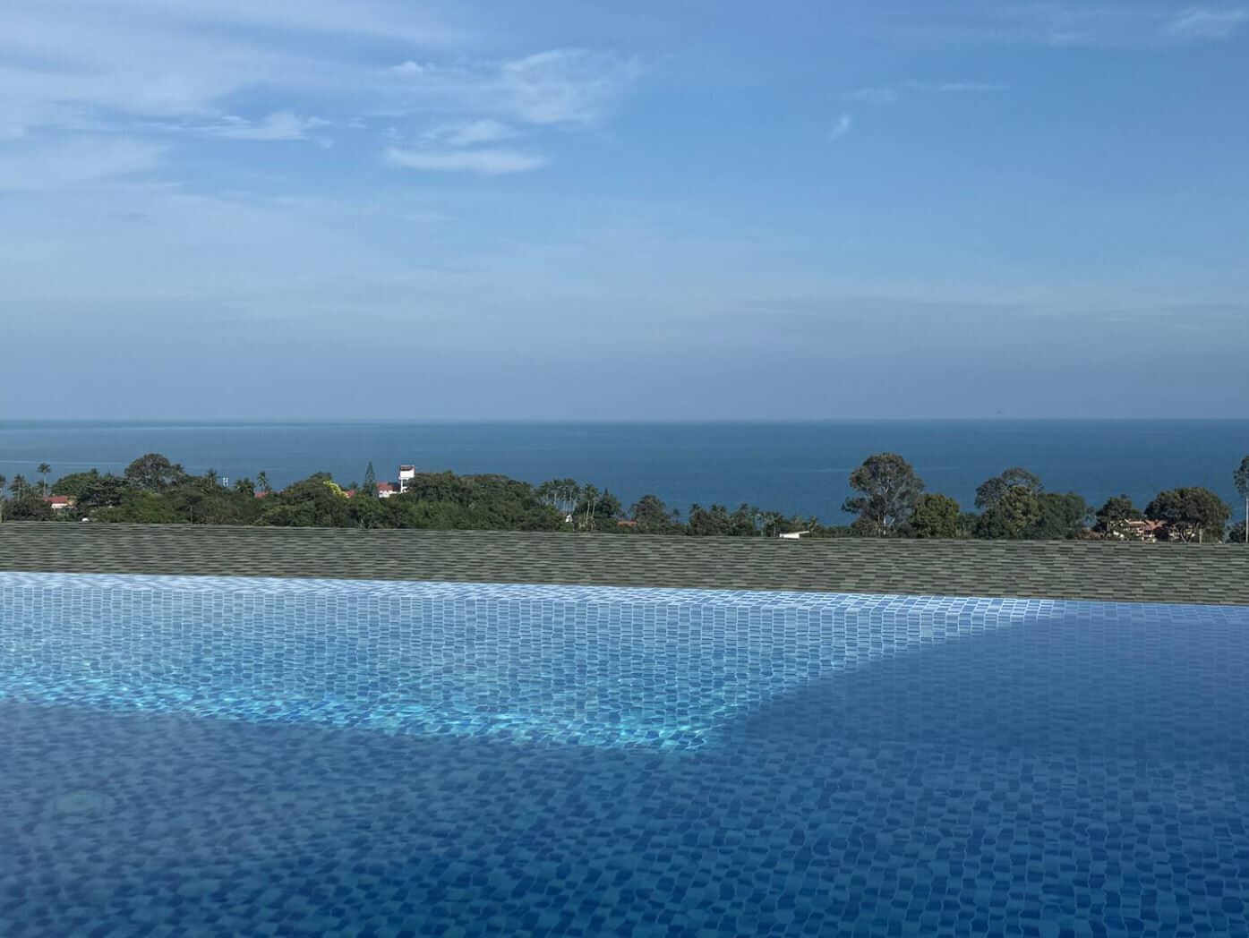 Piscina infinita com vista para o oceano e edifícios ao longe.