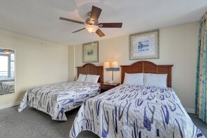 Ein Hotelzimmer mit zwei Betten, einem Deckenventilator, gerahmten Bildern an der Wand und einem Fenster mit Vorhängen.
