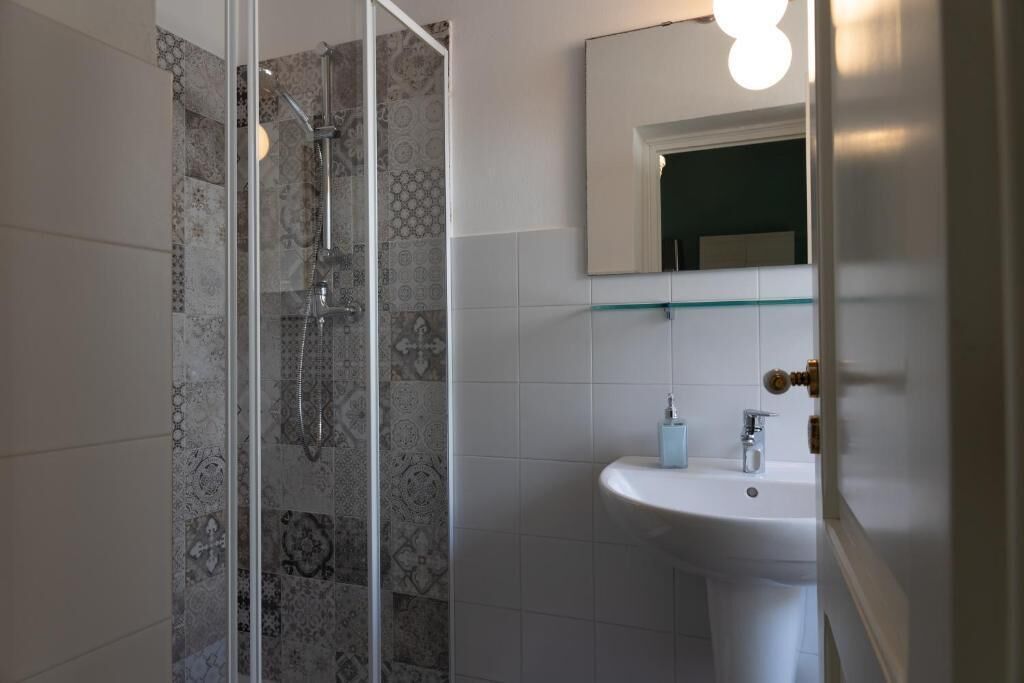 A modern bathroom with a glass shower enclosure, a white sink, and a mirror with a light fixture.