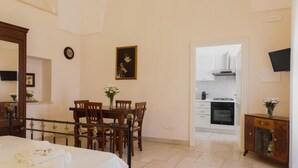 Ein Schlafzimmer mit Bett, Esstisch mit Stühlen, einer kleinen Küchenzeile und einem an der Wand befestigten Fernseher.