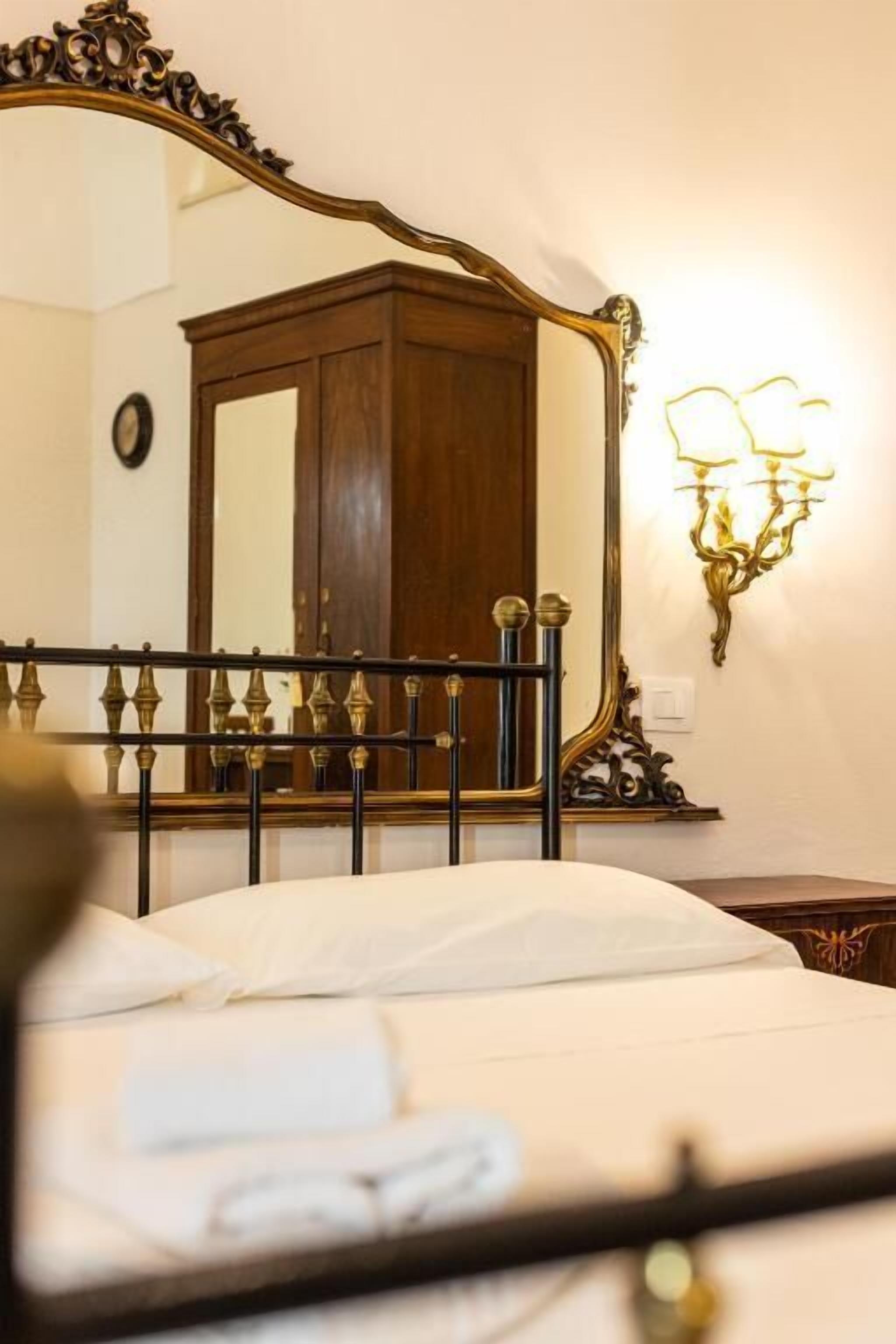 Une chambre d’hôtel avec un lit, un grand miroir, une armoire en bois et un luminaire fixé au mur.