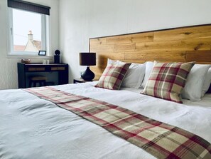 A neatly made bed with a plaid bedspread, a wooden headboard, and a bedside table with a lamp.