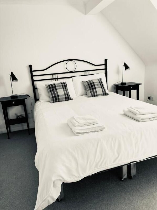 A neatly made bed with white bedding and plaid pillows, a black metal headboard, and two bedside tables with lamps. - The Well Country Inn (Scotlandwell)