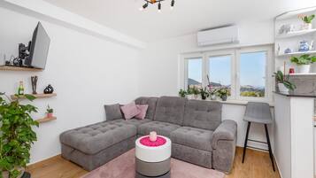 Una sala moderna con un sofá seccional gris, una pequeña mesa redonda con una flor rosa y una zona de bar con un taburete.