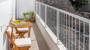 Un balcone con ringhiera bianca, un tavolino con sedie e piante in vaso.