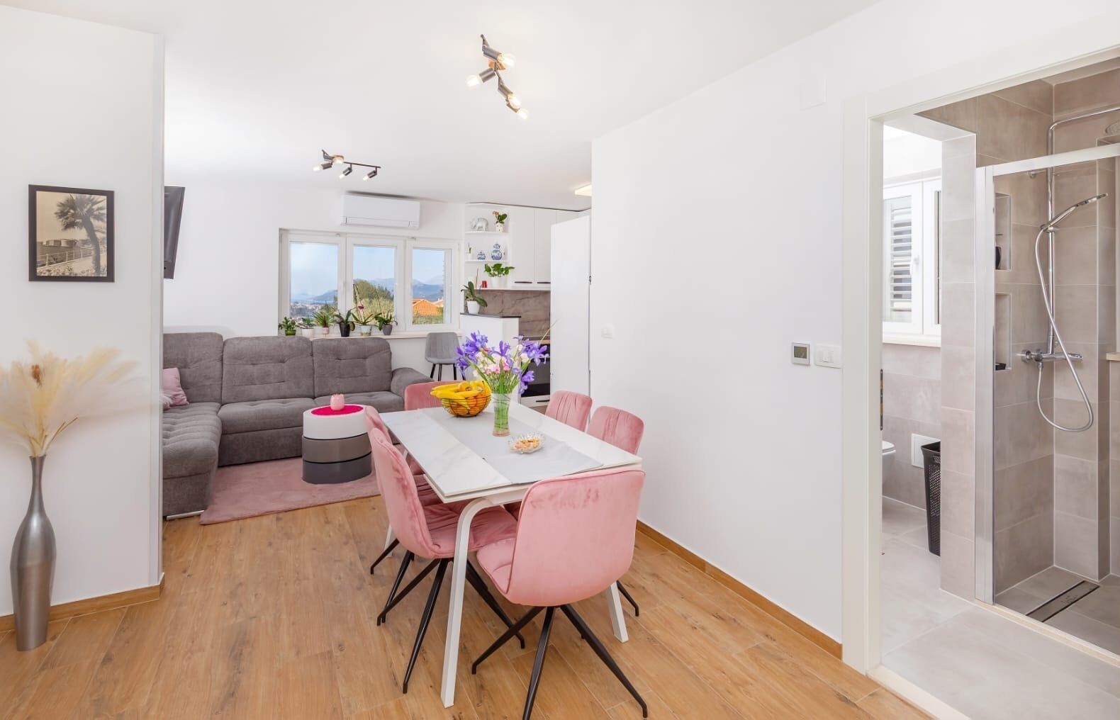 A modern living room with a dining area, a sofa, a table with pink chairs, and a view of the outside.