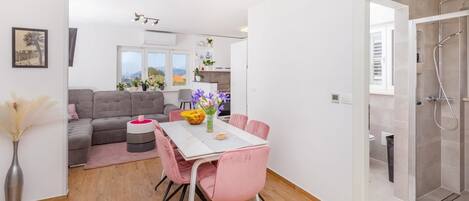 A modern living room with a dining area, a sofa, a table with pink chairs, and a view of the outside.