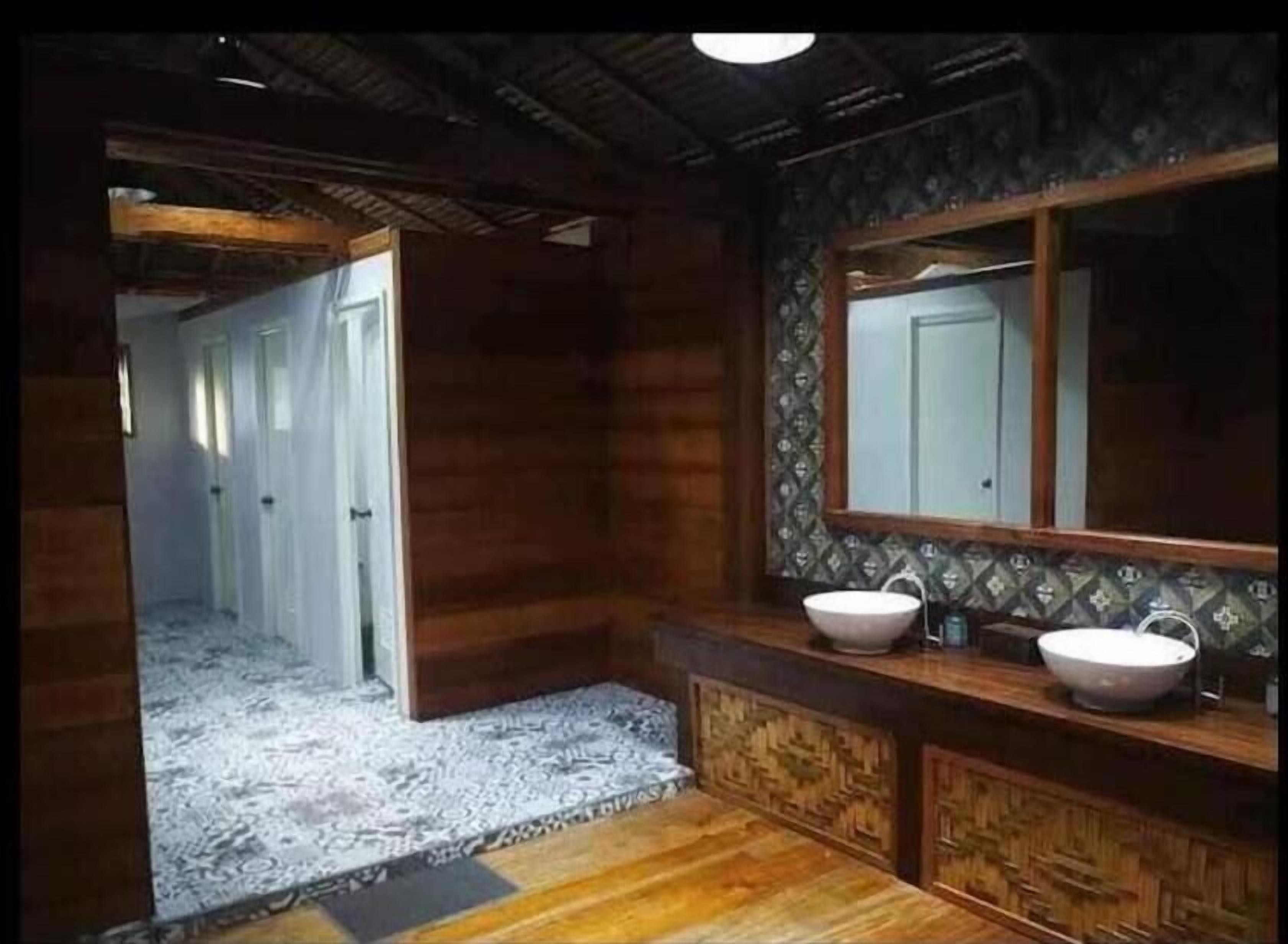 Un baño con tocador de madera, dos lavamanos, un espejo grande y piso estampado.