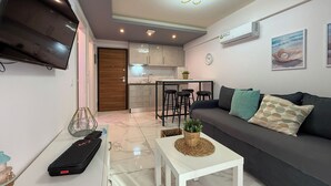 A modern living room with a sofa, a coffee table, and a TV. There is a kitchen area with a dining table and chairs. - Ilektra Suite n. 28 by SDR (Katerini)