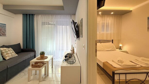 A modern, well-lit bedroom with a bed, bedside table, and a small seating area with a sofa and a table. - Ilektra Suite n. 28 by SDR (Katerini)