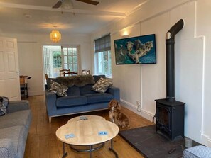 Een woonkamer met een bank, een hond, een tafel, een open haard en een schilderij aan de muur.