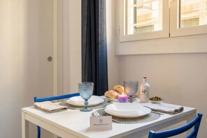 Uma mesa de jantar posta com pratos, copos, uma vela, uma garrafa e croissants, com uma placa indicando 'TIMELESSPUCLIA.COM'.