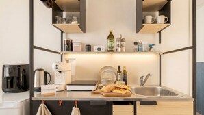 Pieni ja käytännöllinen keittiö, jossa on kahvinkeitin, vedenkeitin, leivänpaahdin, pesuallas sekä hylly, jossa on purkkeja ja pullo.