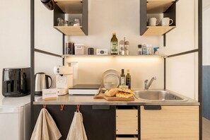Uma cozinha compacta com cafeteira, chaleira, torradeira, pia e uma estante com potes e uma garrafa.