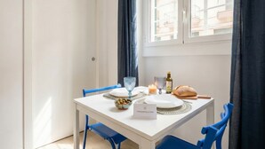 Una mesa de comedor dispuesta con platos, vasos, un cuenco de aceitunas, pan y una vela.