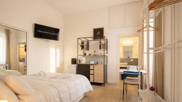 Hotellihuone, jossa on sänky, työpöytä, tuoli, televisio ja peili.
