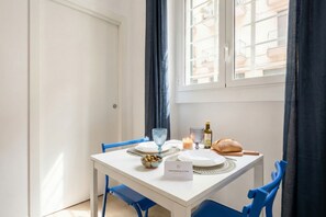 Una mesa de comedor dispuesta con platos, vasos, un cuenco de aceitunas, pan y una vela.