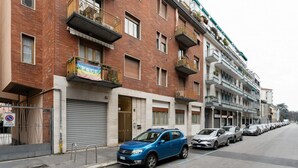 A multi-story residential building with balconies, a closed garage door, and parked cars along the street. - GuestHost - Comfortable and cozy 35 square meters studio apartment, perfect for two people, located on the ground floor of a building.The property is located near the Gambara M1 metro station (5 minutes' walk), offering quick access to Milan's most centr (Milan)