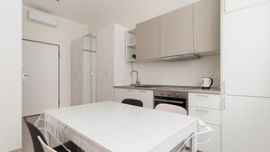 A compact kitchen with white cabinets, a stove, a sink, and a dining area with a table and chairs. - GuestHost - Comfortable and cozy 35 square meters studio apartment, perfect for two people, located on the ground floor of a building.The property is located near the Gambara M1 metro station (5 minutes' walk), offering quick access to Milan's most centr (Milan)