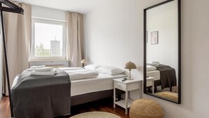 Una habitación de hotel con cama, mesita de noche, lámpara, un reposapiés redondo y un espejo grande en la pared.
