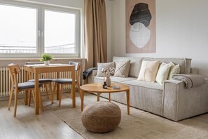 A living room with a sofa, a round coffee table, a dining table with chairs, and a large window with curtains. - Global Living München Olympiapark (Munich)