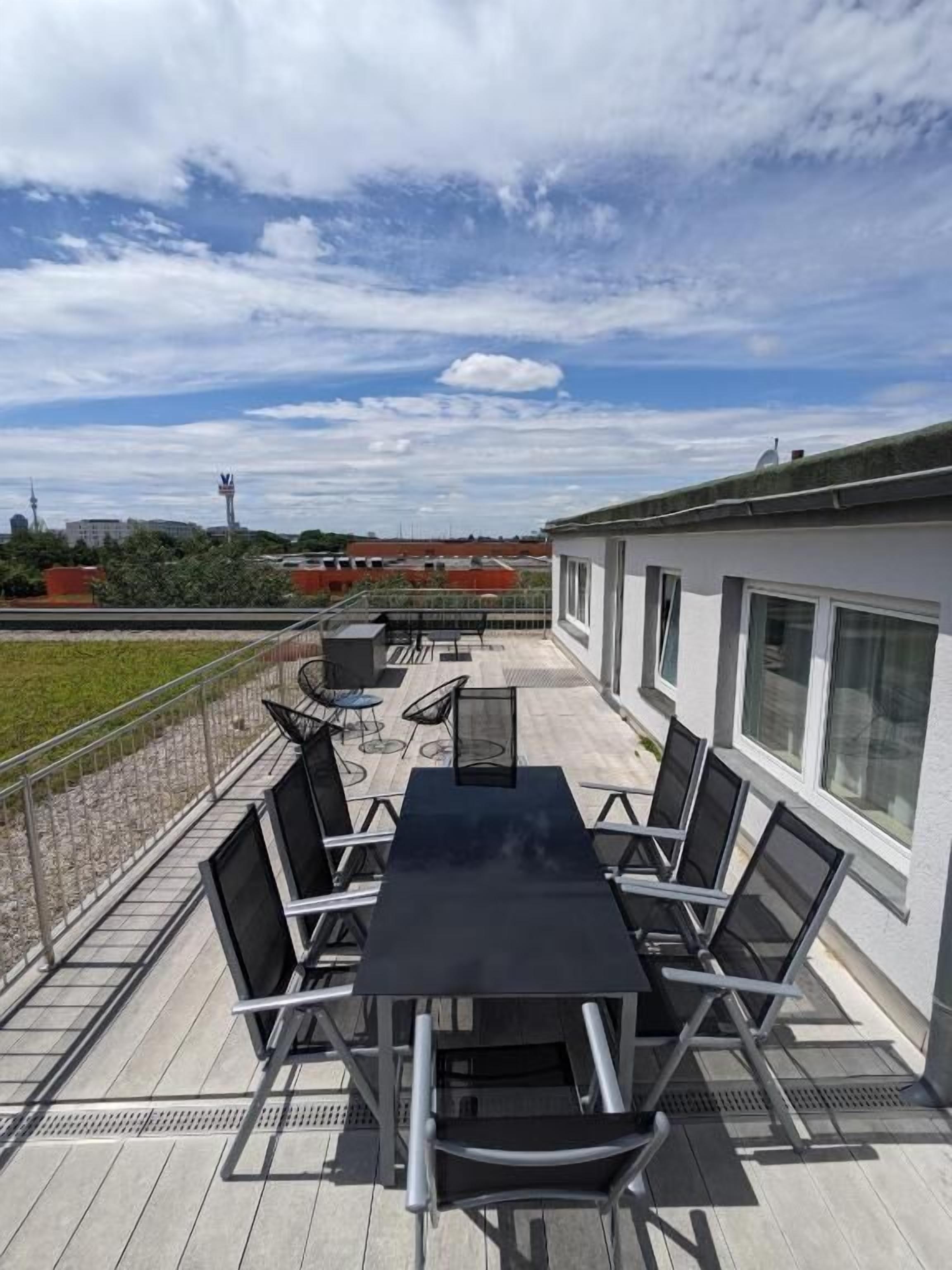 A rooftop patio with a black table and chairs, a small seating area, and a view of the cityscape.