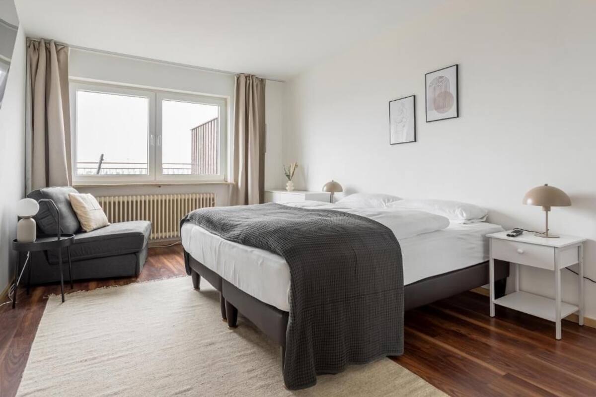 A modern bedroom with a large bed, a bedside table, a chair, and a window with curtains.