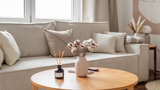 Una sala de estar moderna con un sofá color beige, una mesa de centro redonda de madera y un jarrón con flores secas.