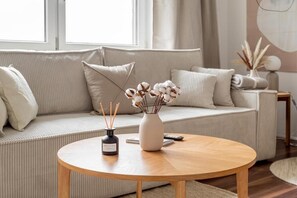 A modern living room with a beige sofa, a round wooden coffee table, and a vase with dried flowers. - Global Living München Olympiapark (Munich)