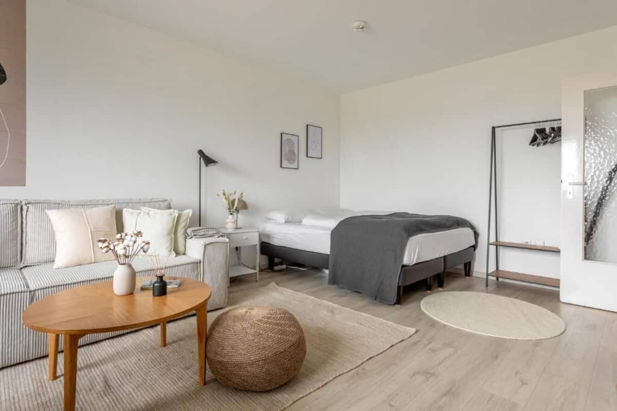 A modern, minimalist bedroom with a bed, a sofa, a coffee table, and a bedside table.