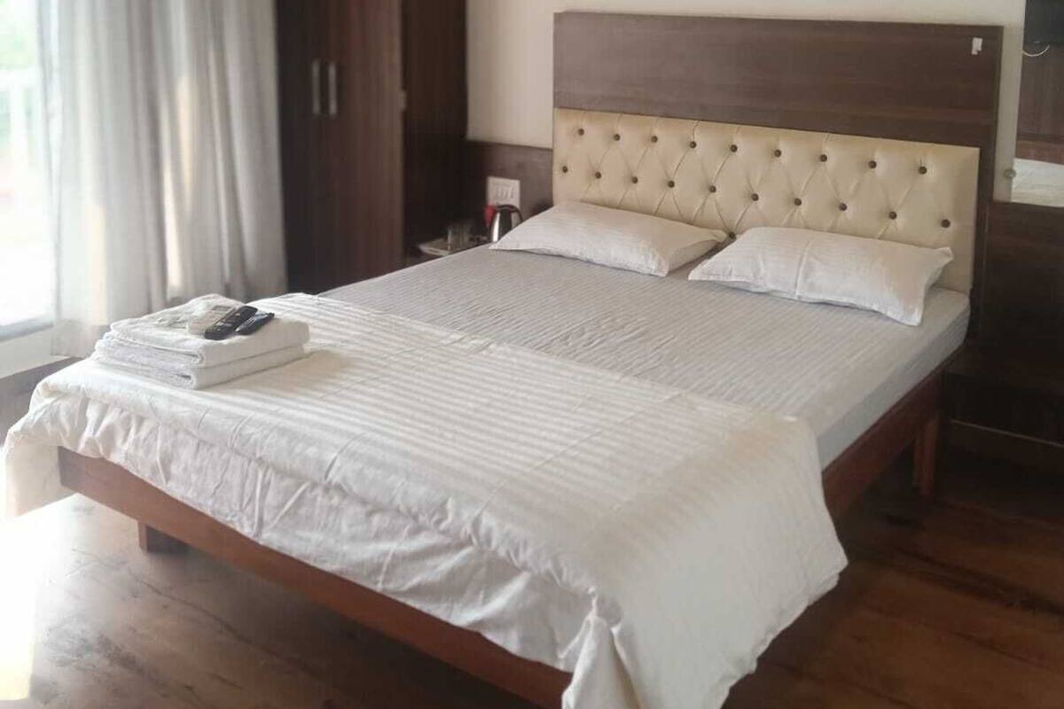 A neatly made bed with a tufted headboard, a wooden wardrobe, and a large window with curtains.