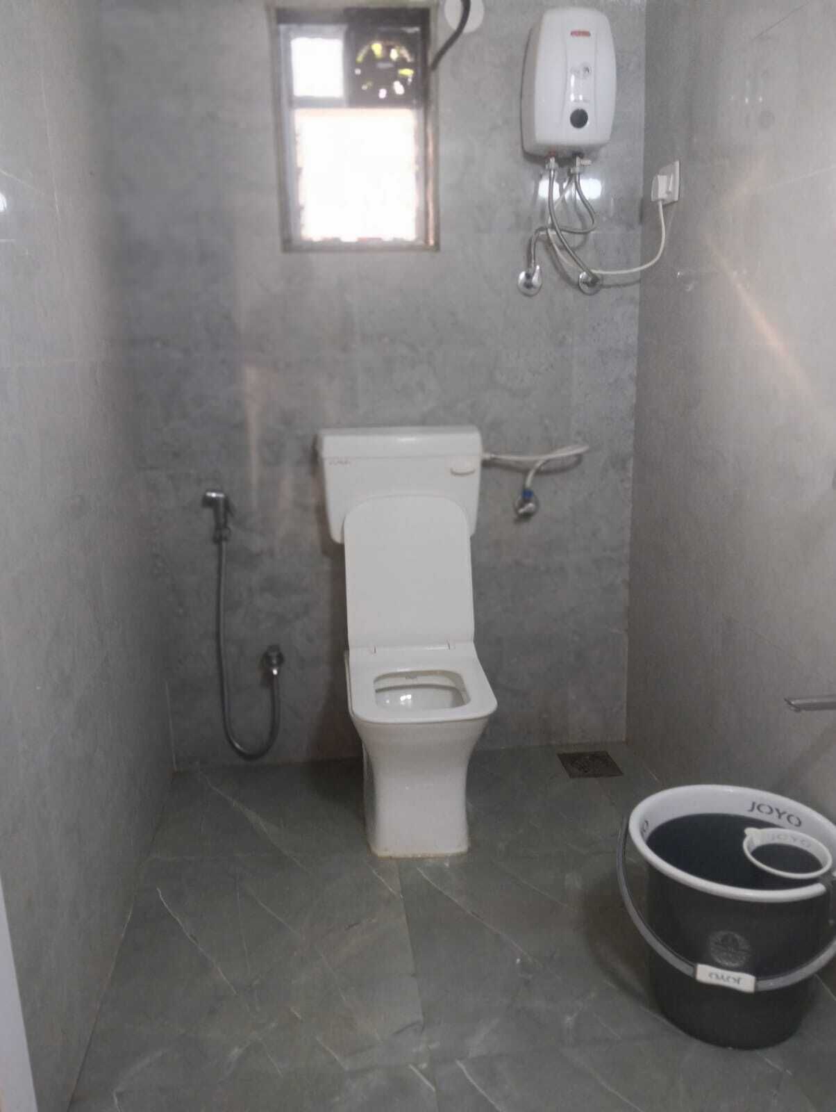 Ein kleines Badezimmer mit Fliesen, einer Toilette, einem Händetrockner und einem Eimer.