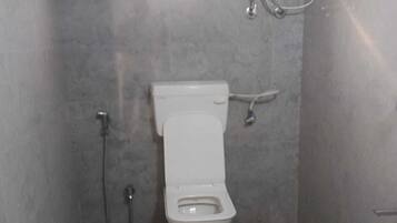 Ein kleines Badezimmer mit Fliesen, einer Toilette, einem Händetrockner und einem Eimer.