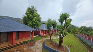 A courtyard with red brick buildings, a stone pathway, and a well-maintained lawn. - Aranyagiri Farm Stay (Rameghar)