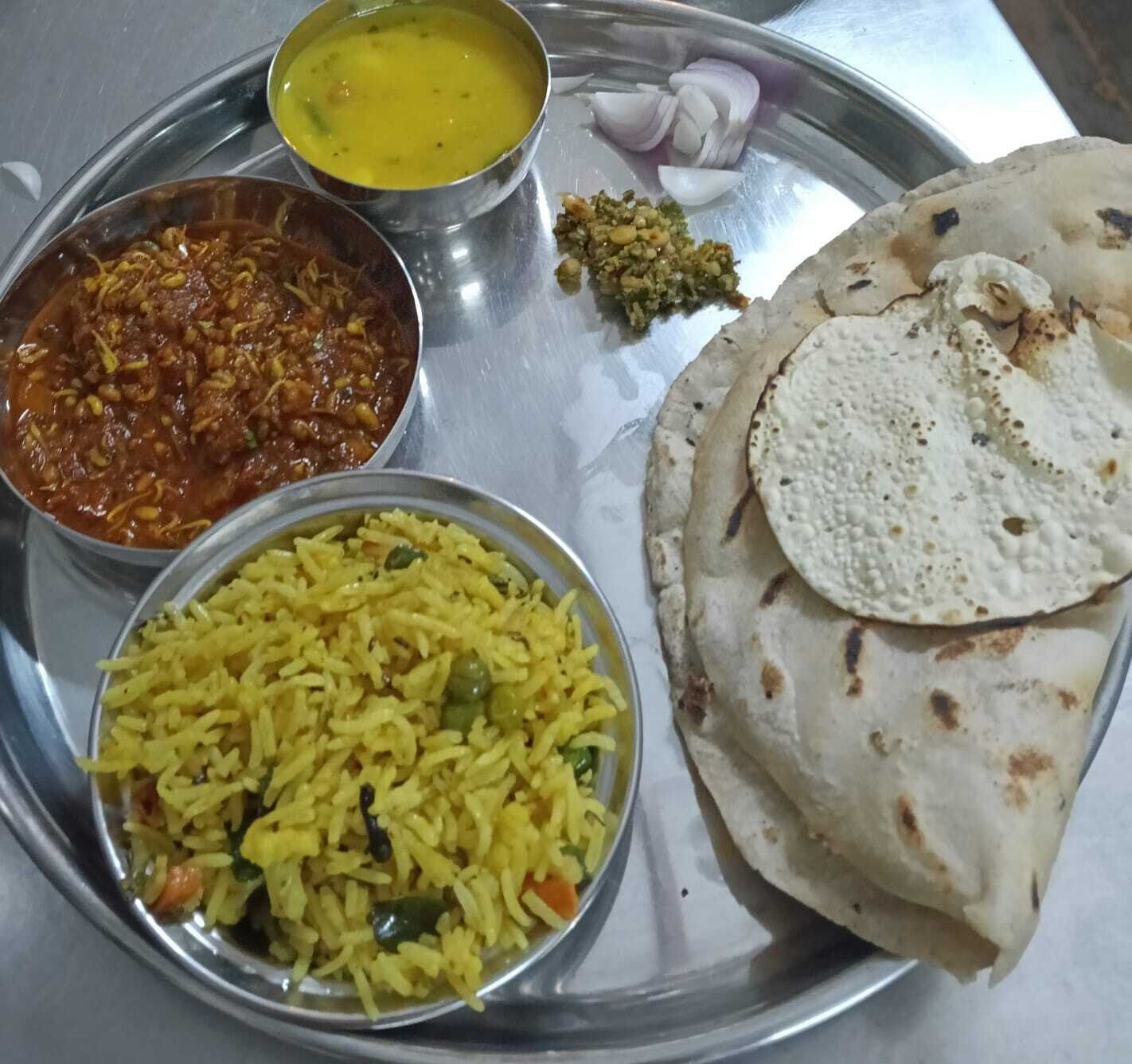 Een maaltijd bestaande uit rijst, curry, een kommetje dal en twee stukken platbrood, geserveerd op een metalen bord.