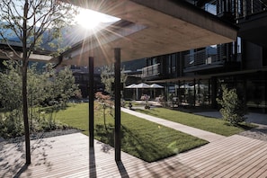 A modern outdoor area with a wooden deck, a grassy lawn, and a covered seating area with umbrellas.