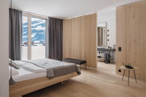 A modern bedroom with a large bed, a bench, a small table, and a mirror.