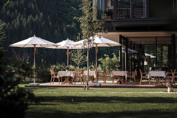 An outdoor dining area with tables and chairs, surrounded by a wooden deck and a view of a forested mountain. - zelloon boutique hotel (Zell am Ziller)