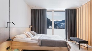 A modern bedroom with a wooden bed, a bench, and a view of mountains through large windows.
