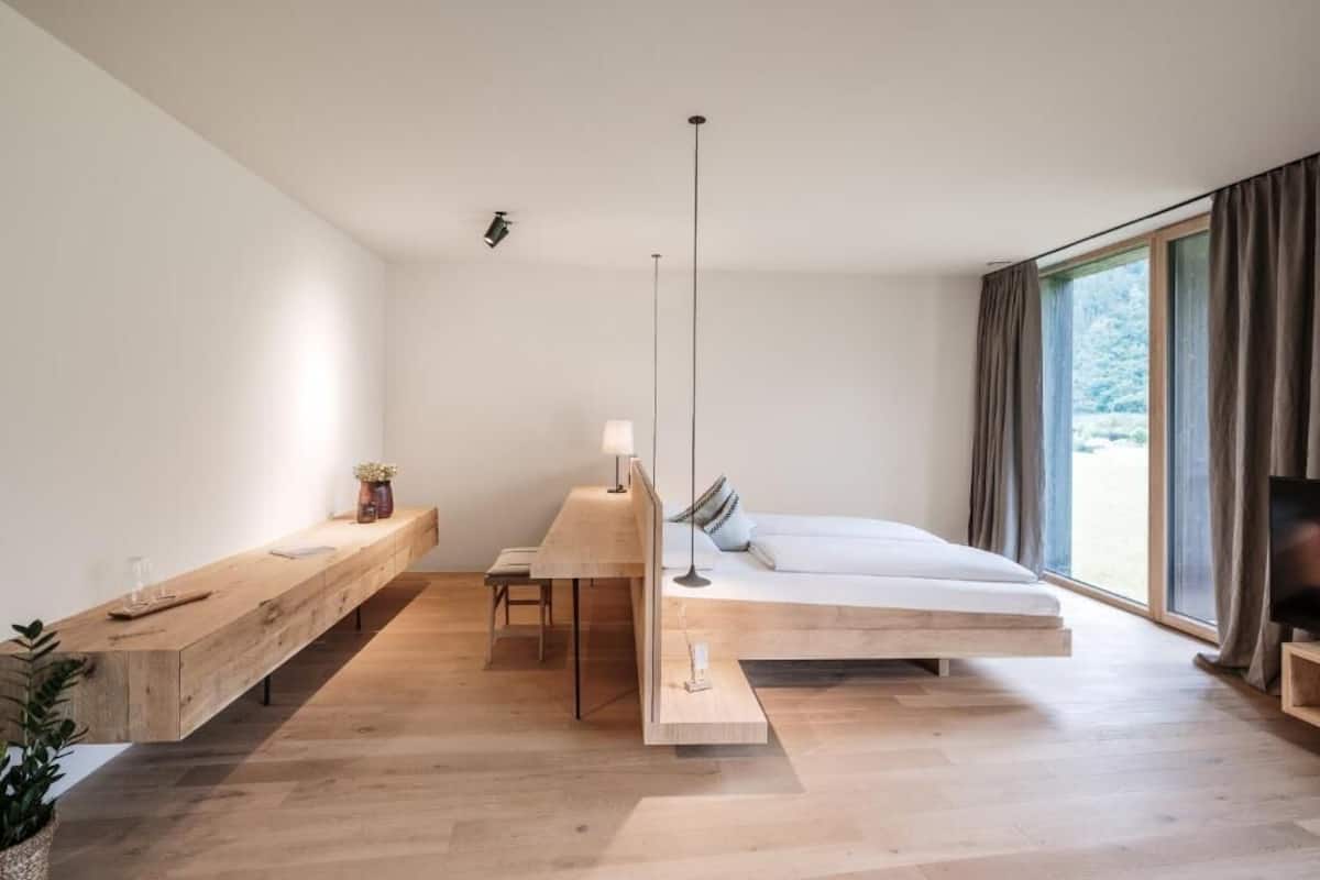 A modern bedroom with a minimalist design, featuring a large bed, a wooden desk, and a large window with curtains.
