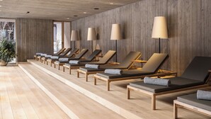 A row of sun loungers with cushions, wooden flooring, and a wooden wall with recessed lighting.