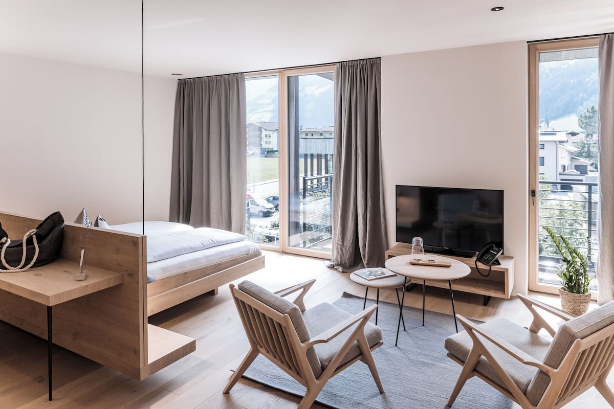 A modern hotel room with a bed, a TV, a desk, and a seating area.